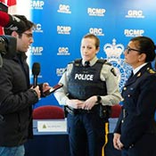Deux agentes de la GRC répondant aux questions d’un journaliste, avec au premier plan une caméra de télévision portant le logo de la CBC.