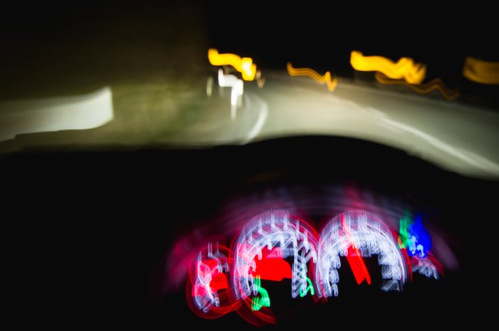 Vue depuis l'intérieur d'un véhicule la nuit. Les lumières floues évoquent une visibilité affaiblie ou réduite.