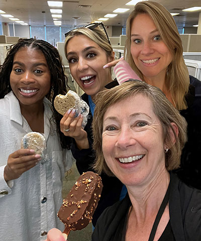 Dans un bureau, quatre femmes tiennent des friandises glacées et sourient à la caméra.