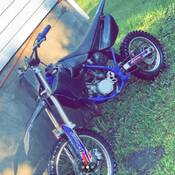 Une moto hors route bleue et noire appuyée contre les fondations d’un bâtiment.