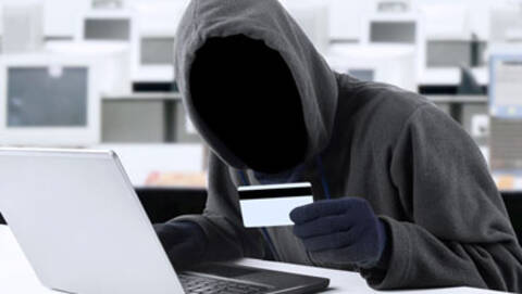 Homme sans visage devant un ordinateur; il tient une carte dans la main. 